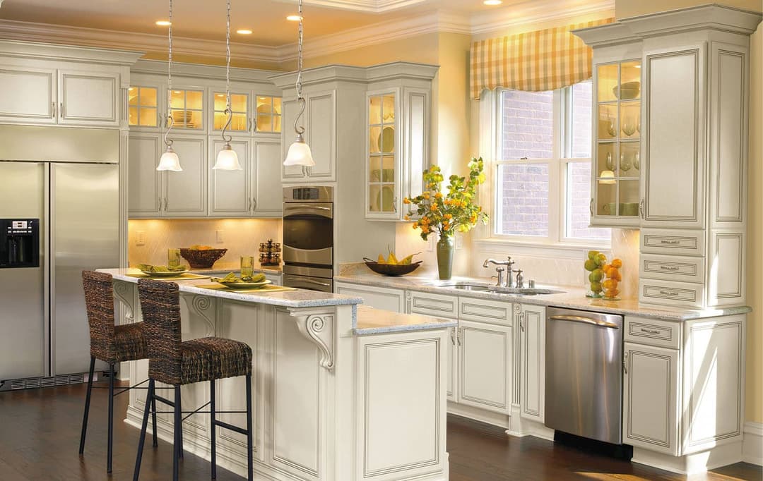 Cream painted kitchen with island seating, glass-front cabinetry and pendant lighting remodeled by Seghi Renovations